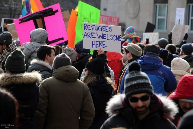 Crowd in winter clothing holds signs, including one reading “Refugees Are Welcome Here.”