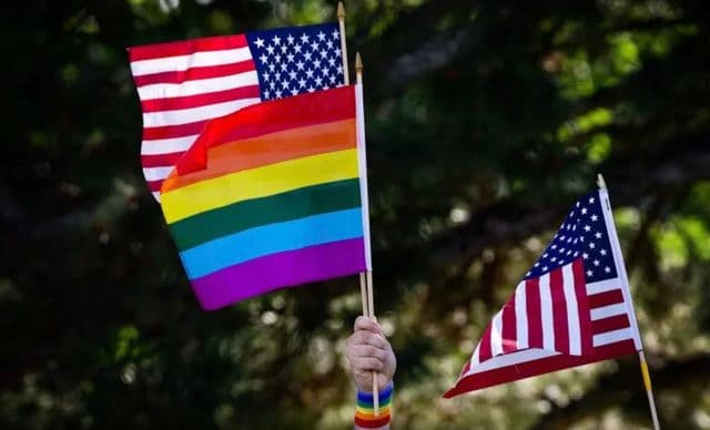 Hand wearing a rainbow bracelet holding Pride flag and USA Flag.