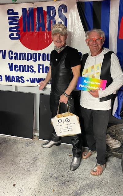 Two people smiling together at an event holding a Rainbow Railroad sign.