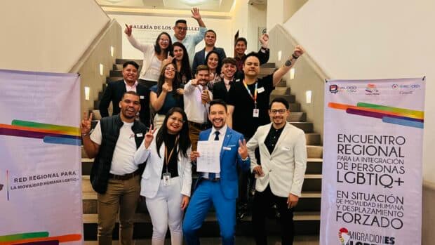Group posing on a staircase holding a document, celebrating at an LGBTIQ+ regional gathering.