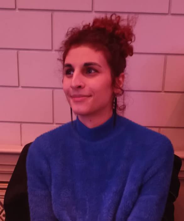 Person in a blue sweater sitting indoors with a calm expression.