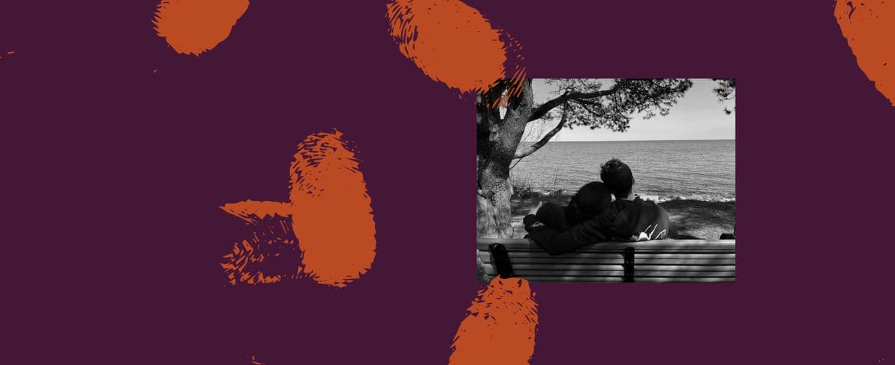 Two people sitting on a bench by the water, one resting their head on the other's shoulder.