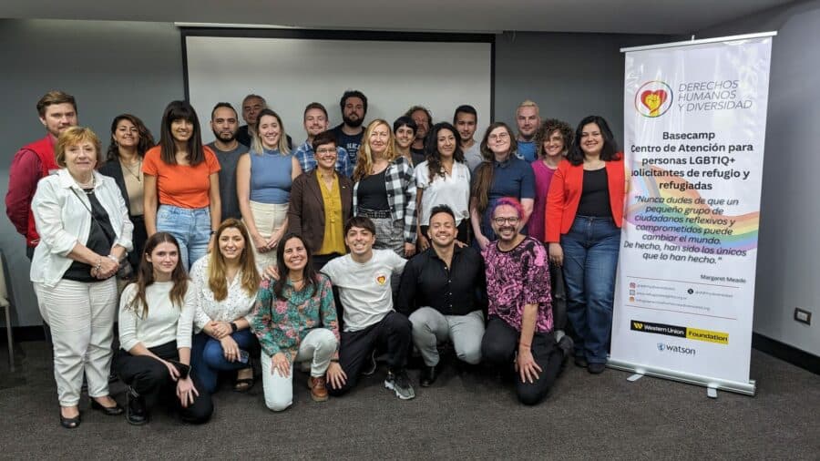 Large group of people posing in front of a whiteboard with a banner labelled "DERECHOS HUMANOS Y DIVERSIDAO"