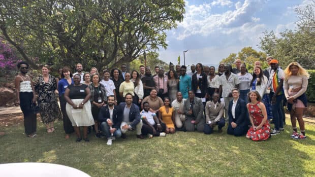 Group of people posing together outdoors on a sunny day with trees and grass in the background.