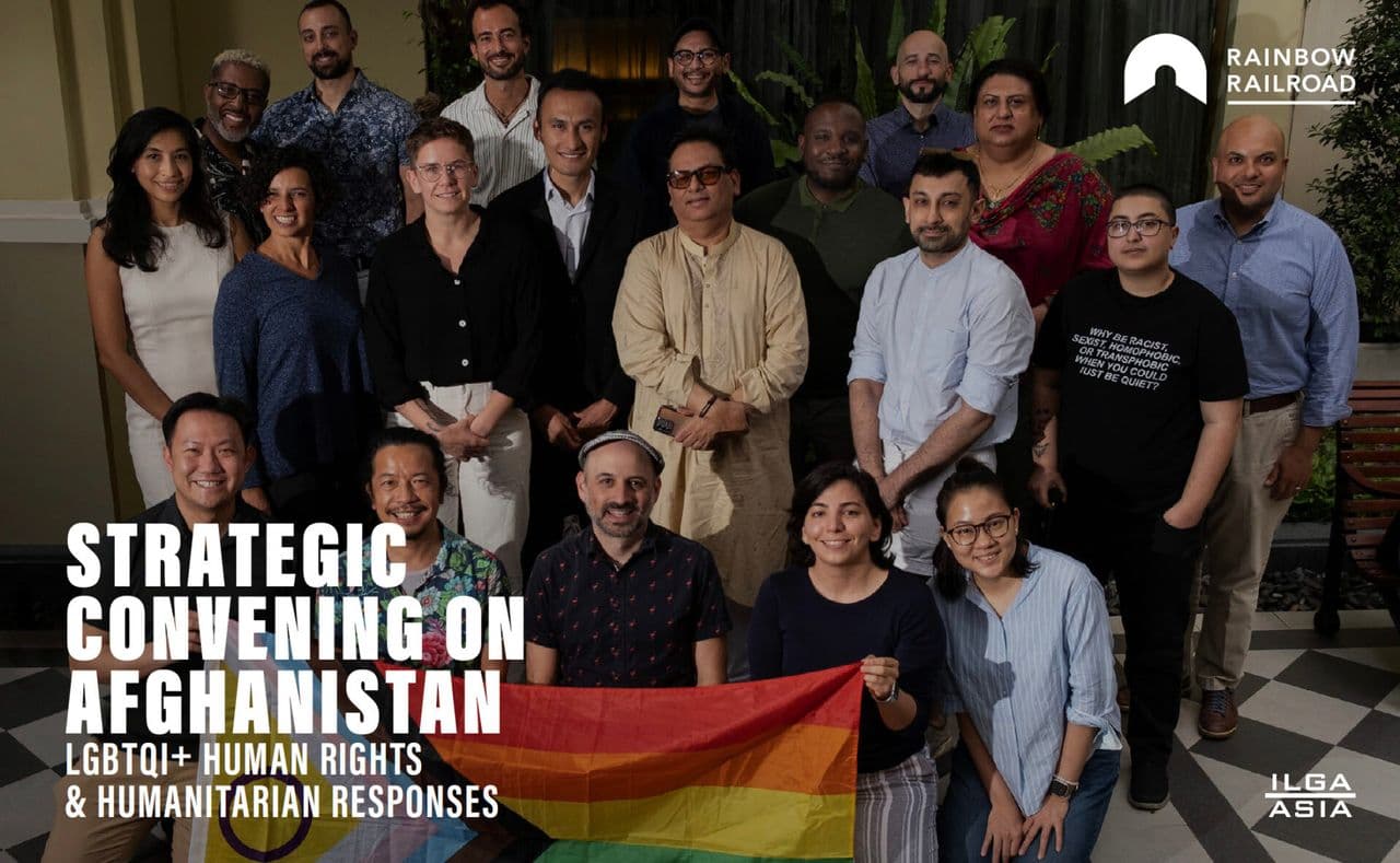 Group of people holding a rainbow flag with the text "Strategic Convening on Afghanistan" in white.