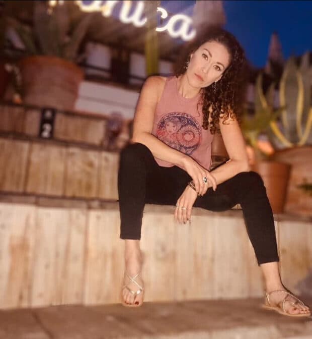 Person seated on wooden steps at night, wearing a sleeveless top and sandals.