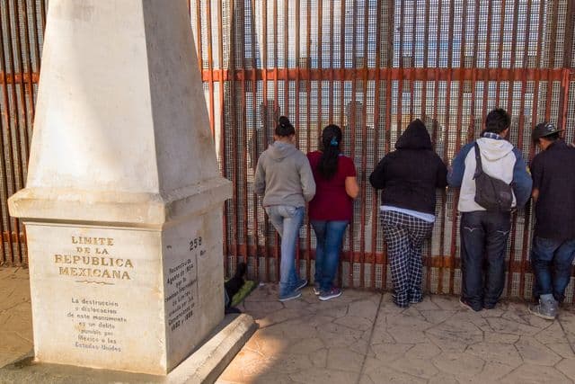 Five people standing near a tall border fence.
