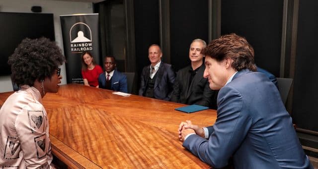 People seated around a conference table in discussion, with a Rainbow Railroad banner visible in the background.