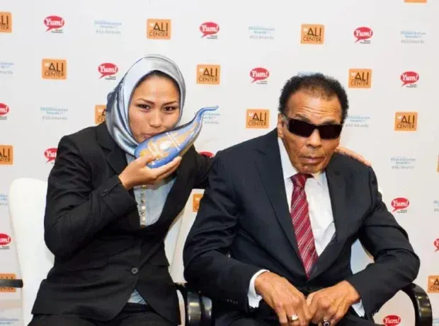 Zahra holding an award sitting beside Muhammad Ali.