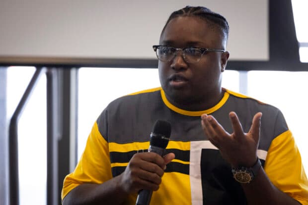 Person speaking into a microphone while gesturing with their hand.