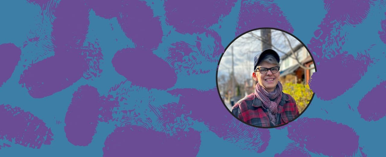 Person smiling outdoors wearing glasses, a cap, and a scarf.