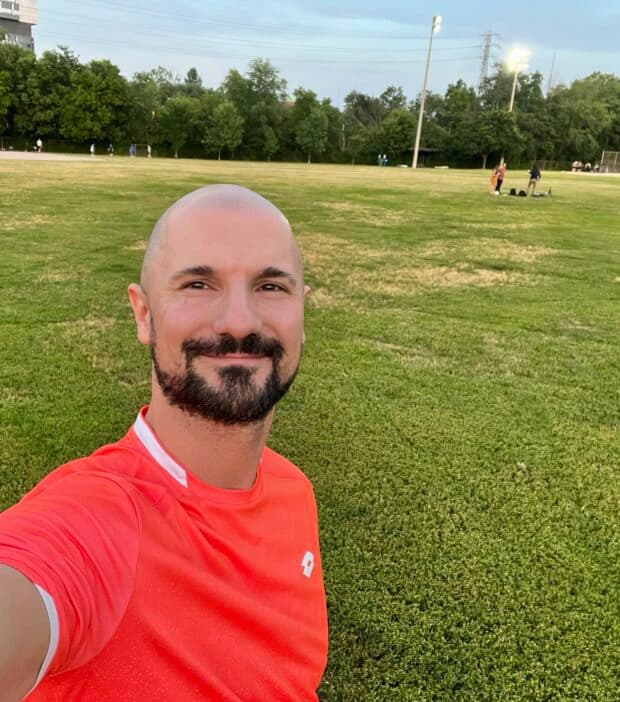 Person in an orange shirt against a grassy background with trees.