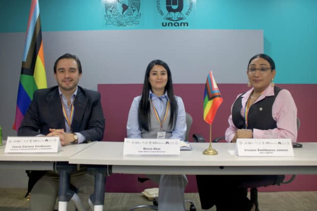 Three panelists seated at a table with nameplates and a small pride flag, in front of a teal wall with UNAM logos.