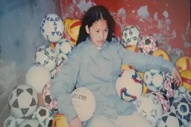 Young person sitting surrounded by many soccer balls.